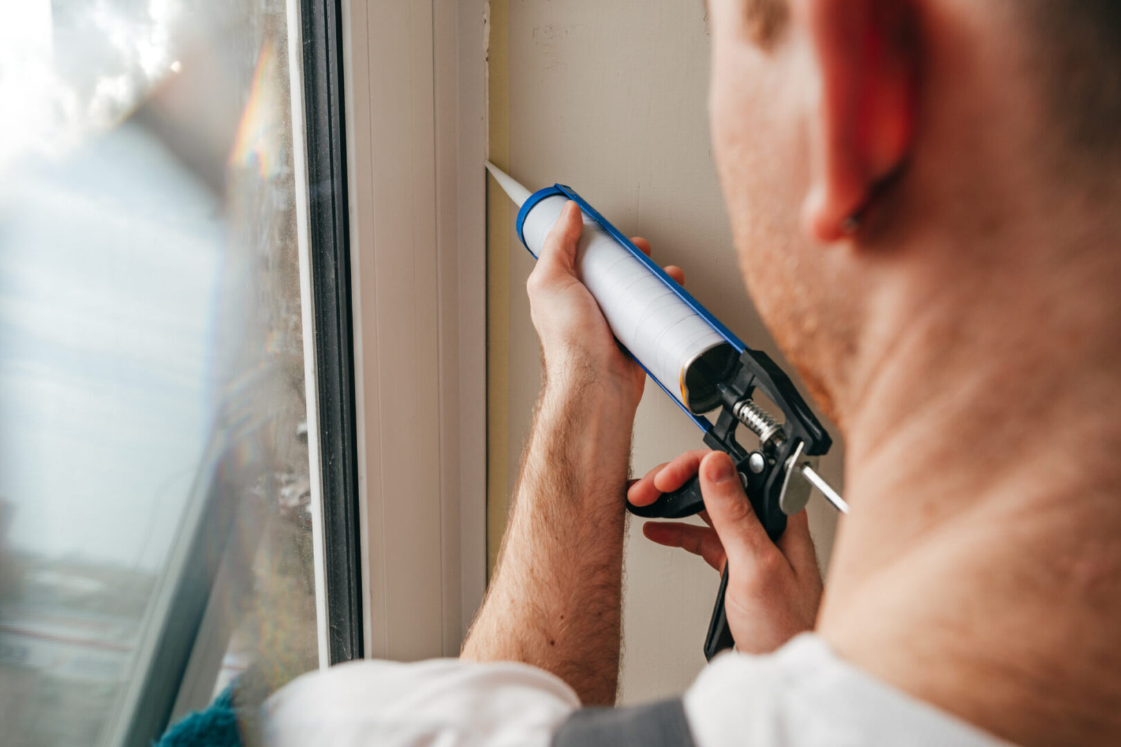 Person applying sealant to a window frame using a caulking gun.