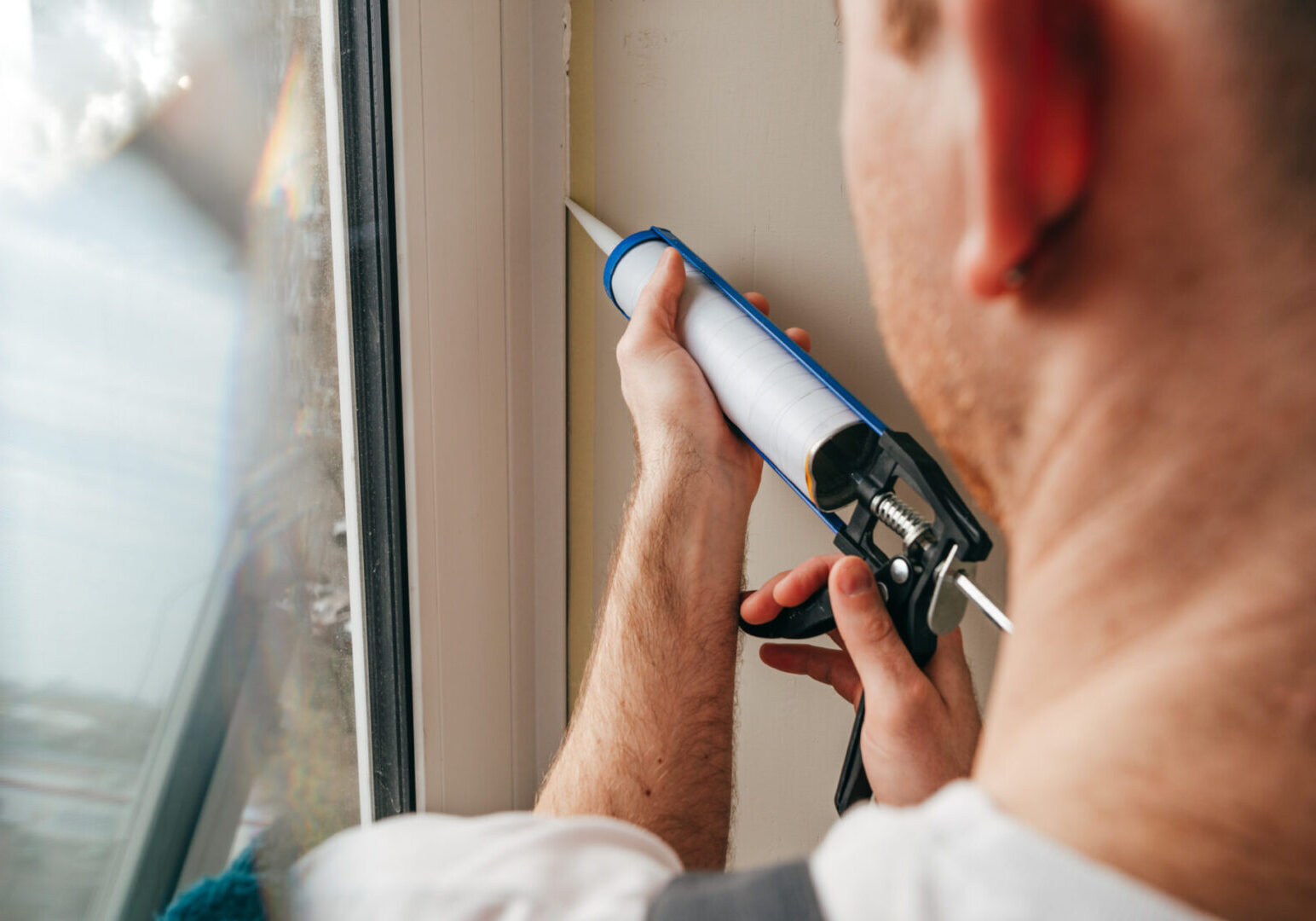 Person applying sealant to a window frame using a caulking gun.